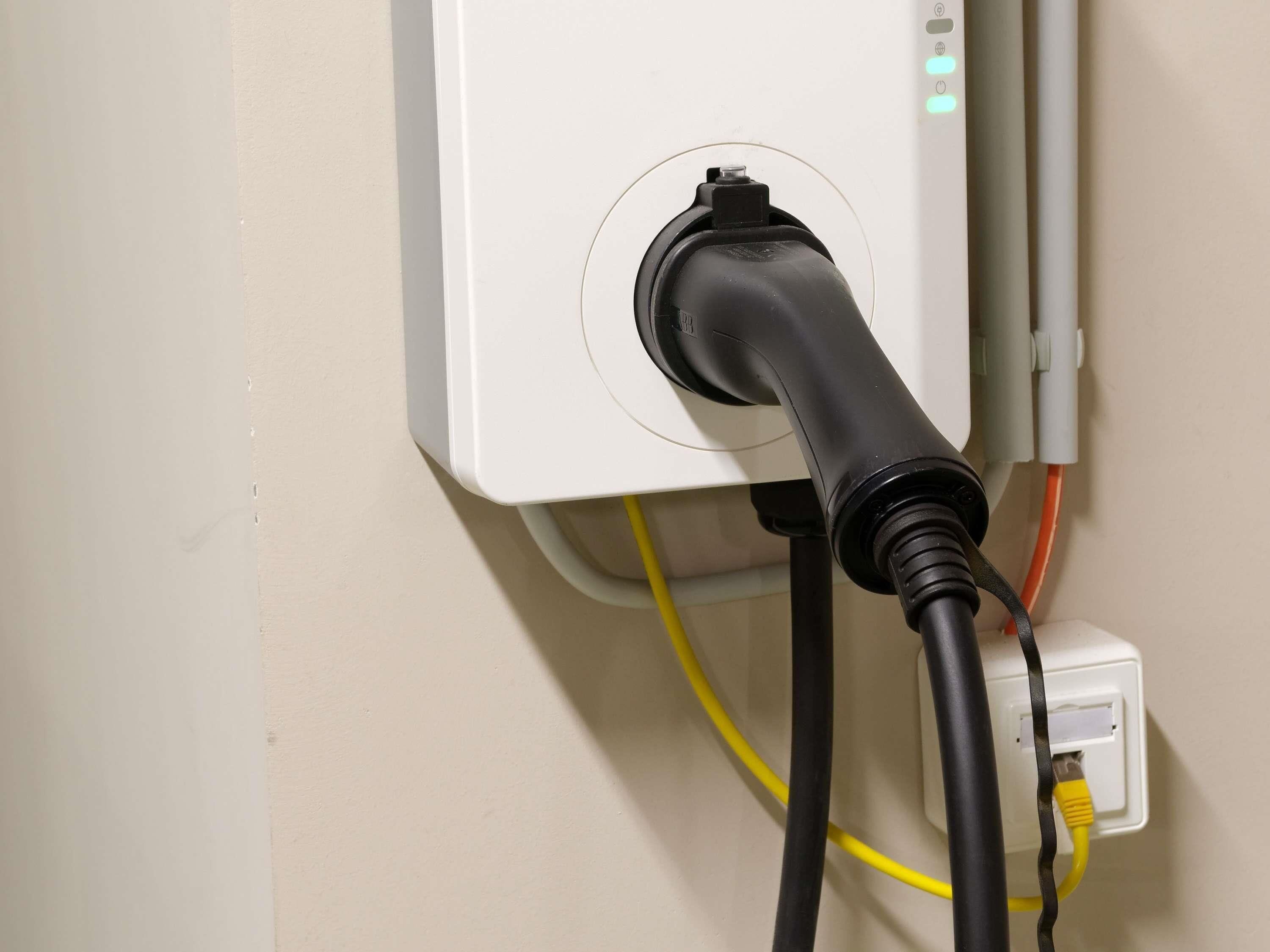 A power outlet with a black cable plugged in, a yellow cable connected to a wall socket, and a white electrical box with a switch.