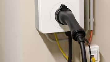 A power outlet with a black cable plugged in, a yellow cable connected to a wall socket, and a white electrical box with a switch.