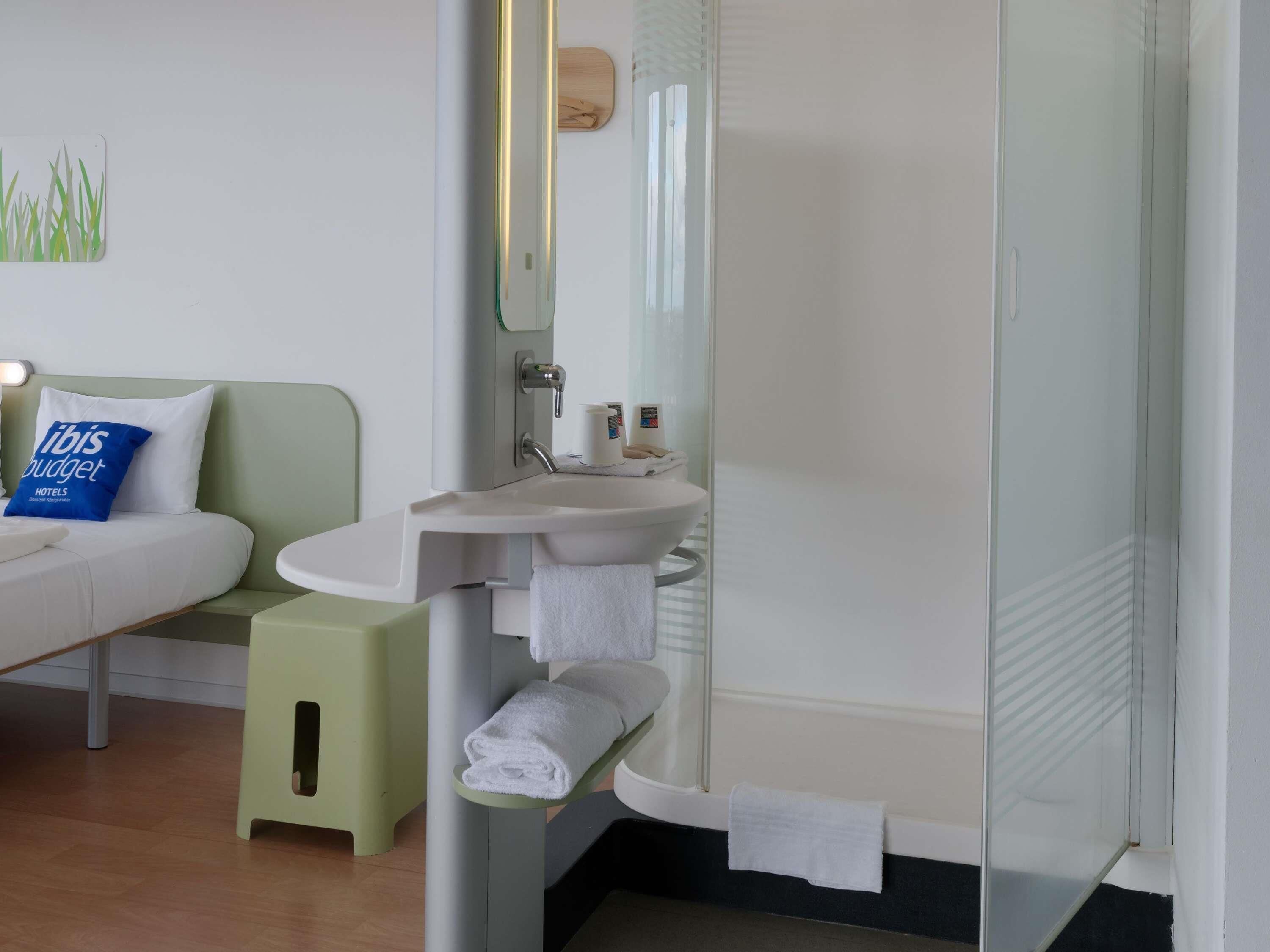 Een moderne badkamer met een douchecabine van glas, een wit wastafeltje en een klein krukje.