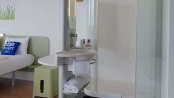 A modern bathroom with a glass shower enclosure, a white sink, and a small stool.