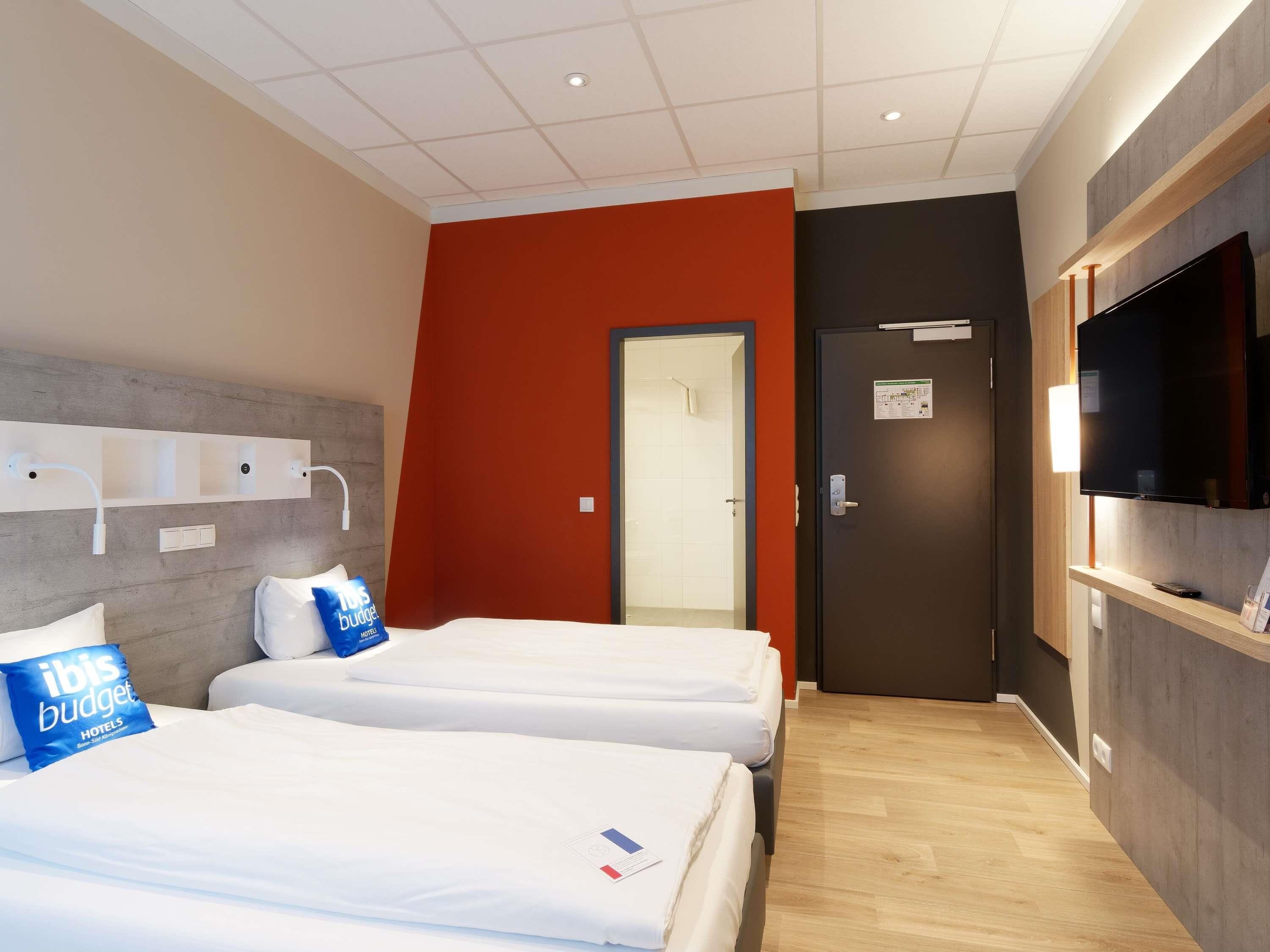 A hotel room with two beds, a TV, a wardrobe, and a bathroom door.