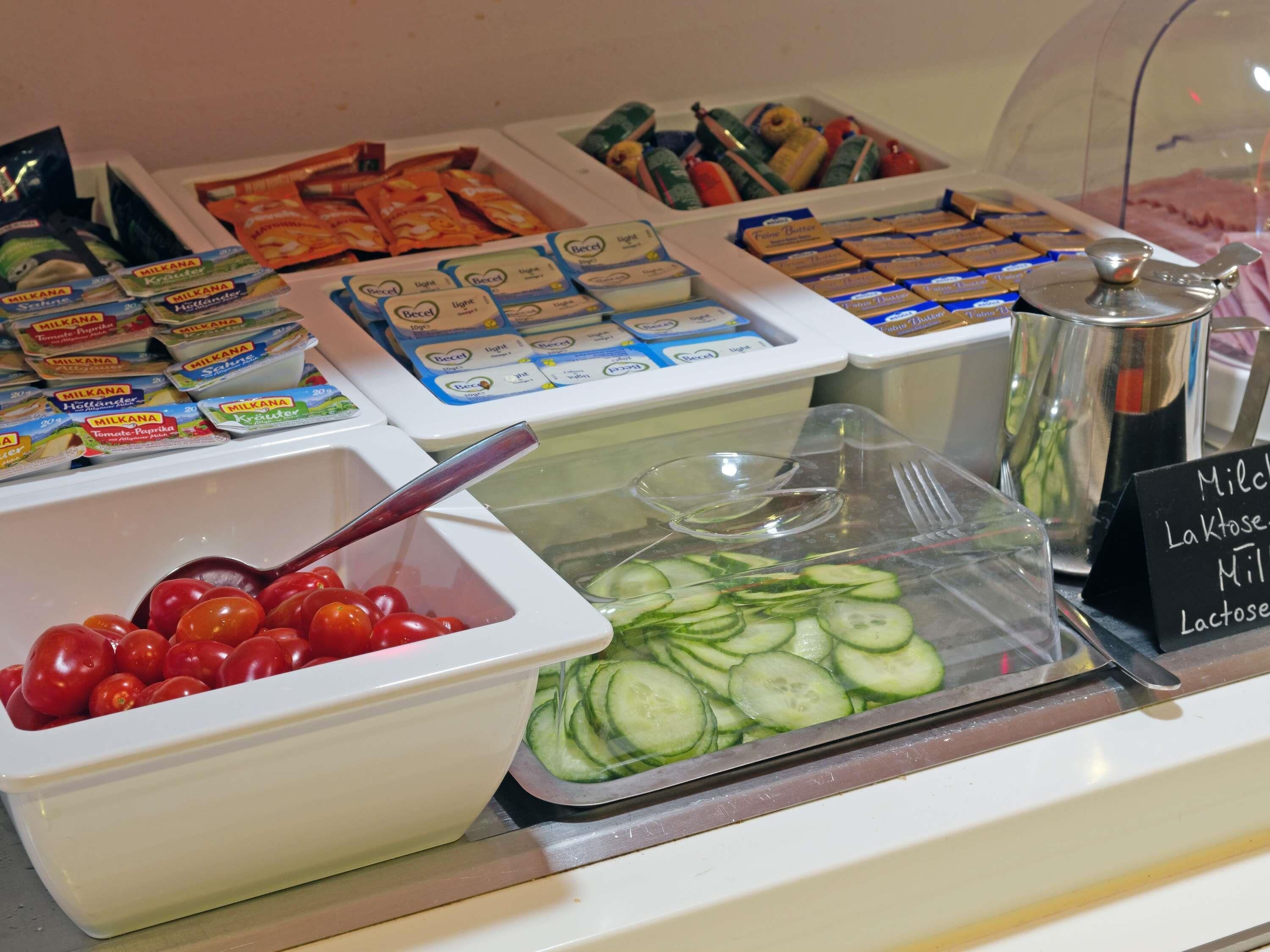 A food display with various dairy products, fresh tomatoes, and sliced cucumbers.