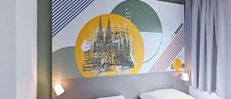 A hotel room with a bed, a nightstand, and a wall-mounted artwork depicting a cityscape.