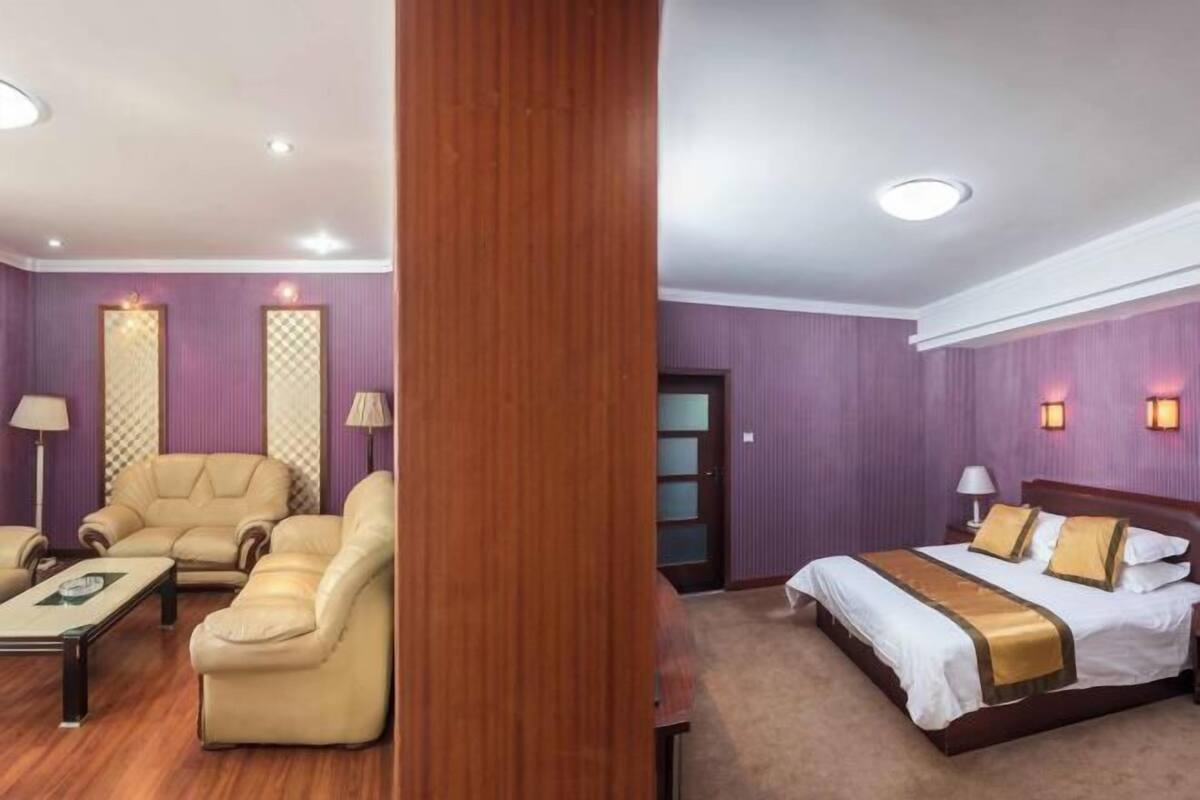 Hotellihuone, jossa on puulattia, kultaisilla yksityiskohdilla koristeltu sänky, sohvaryhmä ja työpöytä.