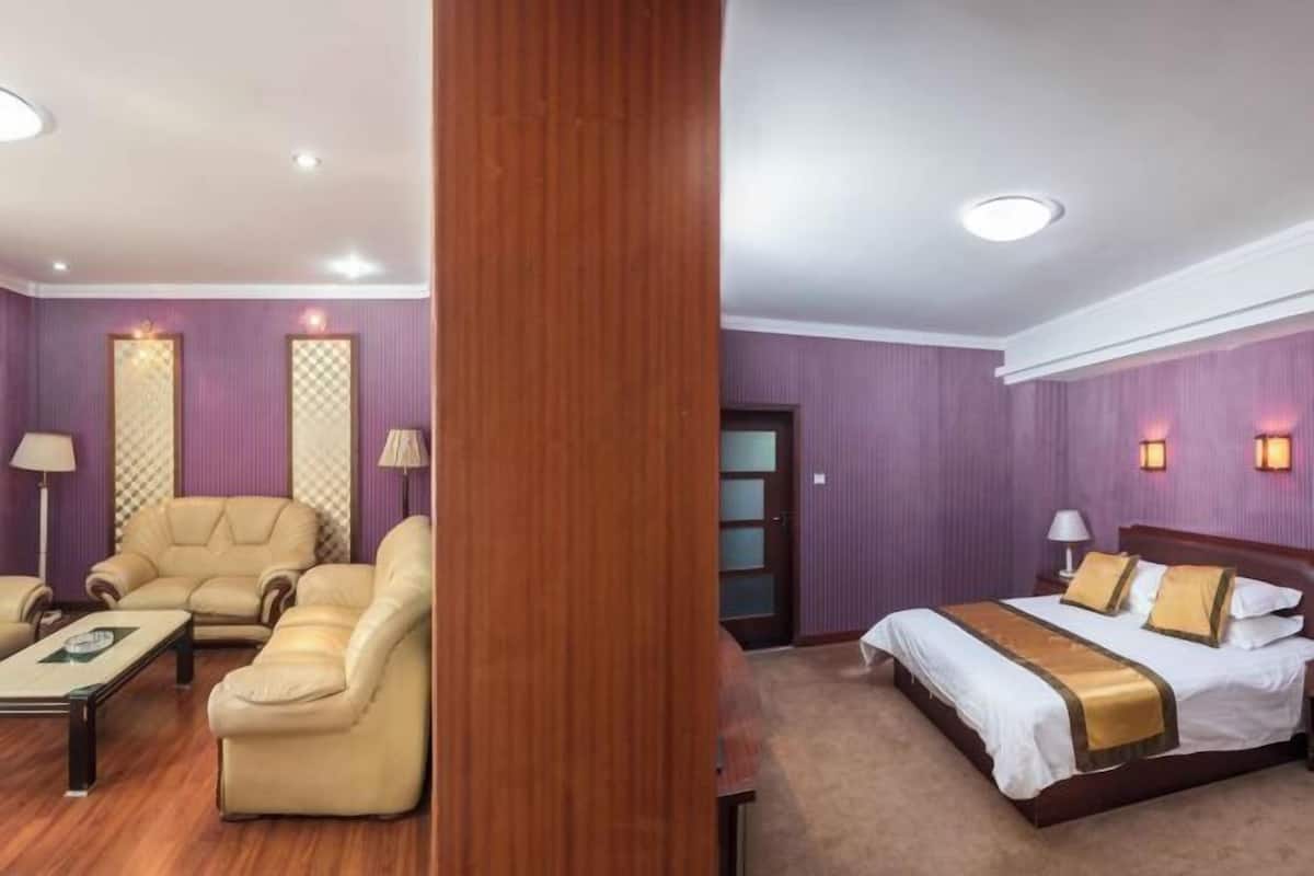 A hotel room with a wooden floor, a bed with a gold accent, a sofa set, and a desk.