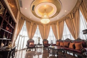 Een luxe kamer met een grote bank, versierde stoelen, een kroonluchter en een groot raam met gordijnen.