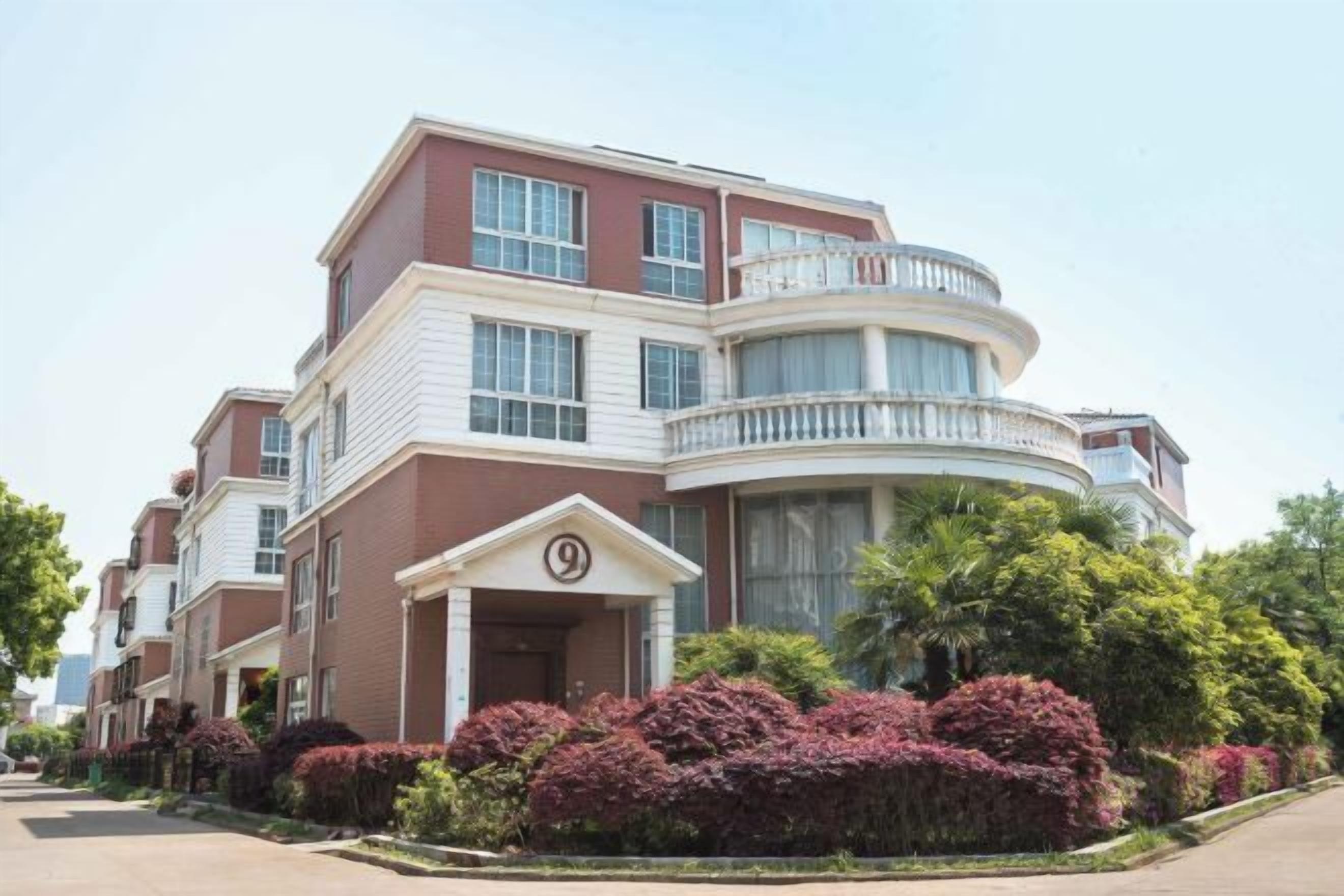 A multi-story residential building with a curved balcony, a prominent entrance with a number sign, and well-maintained landscaping.