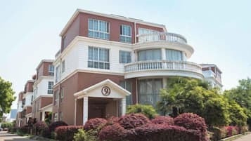 A multi-story residential building with a curved balcony, a prominent entrance with a number sign, and well-maintained landscaping.