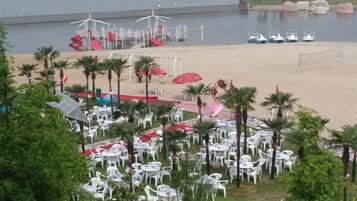 A beachside area with outdoor seating, palm trees, and a view of the beach and water.