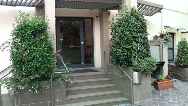 A building entrance with a glass door, steps, and two large potted plants on either side. - 10. Apartment (Signa)