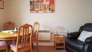 A dining area with a wooden table and chairs, a black leather sofa, and a wall-mounted artwork.