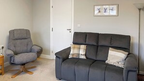 A living room with a grey armchair, a dark grey sofa, and a small wooden side table.