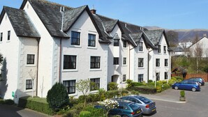 A row of white buildings with dark roofs, parked cars, and a clear sky.
