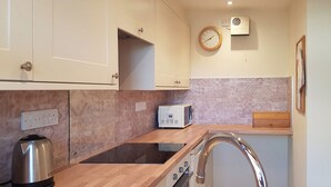A modern kitchen with white cabinets, a stainless steel kettle, a microwave, and a sink.