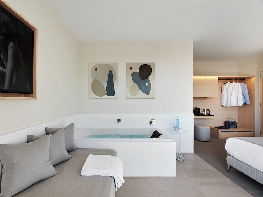 Un dormitorio moderno con una bañera grande, un sofá con cojines y un armario con ropa colgada.