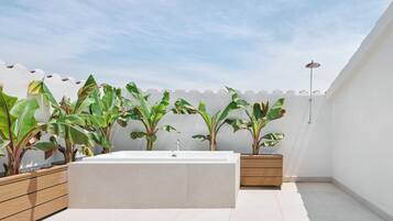 Un baño exterior moderno con una bañera independiente, macetas de madera con plantas tropicales grandes y un diseño minimalista.