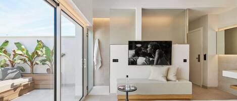 A modern bedroom with a glass door leading to a balcony, a bed, a small round table, and a large mirror.