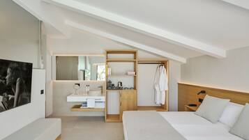 A modern hotel room with a large bed, a bedside table, a built-in desk with a chair, a vanity with a mirror, and a large window.