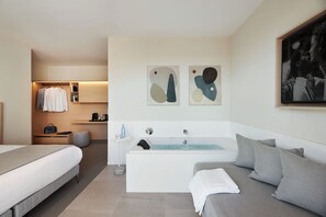 Relax in a serene space with a large bathtub, glass-enclosed shower, and a comfortable grey sofa.