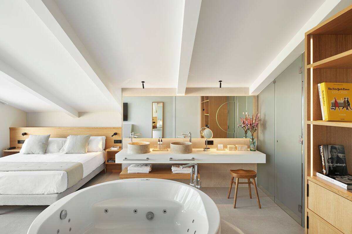 Een moderne slaapkamer met een groot bed, een kaptafel met spiegel, een badkuip en een boekenplank.
