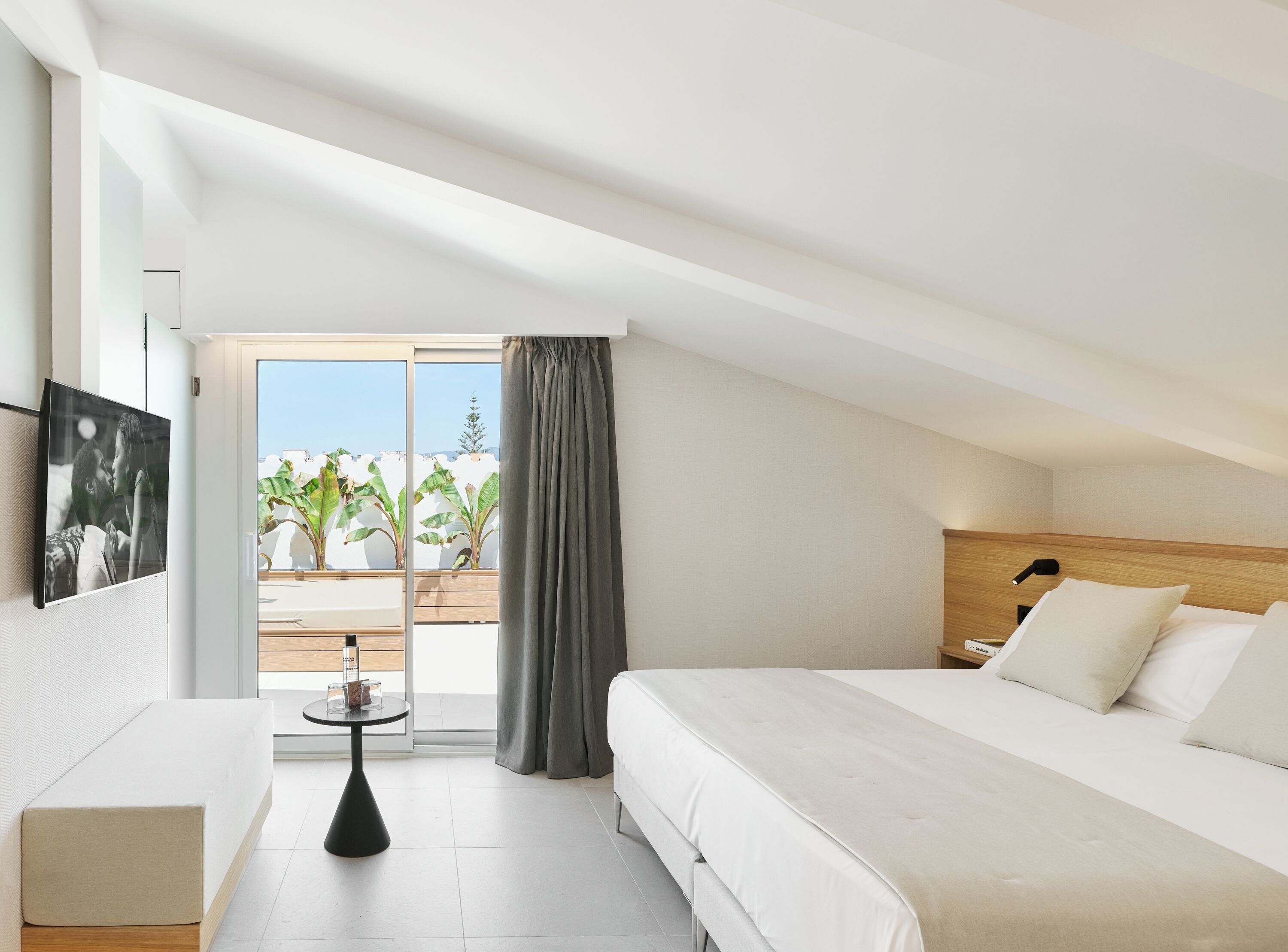 Habitación de hotel moderna con cama, una mesita, televisor y balcón con plantas.