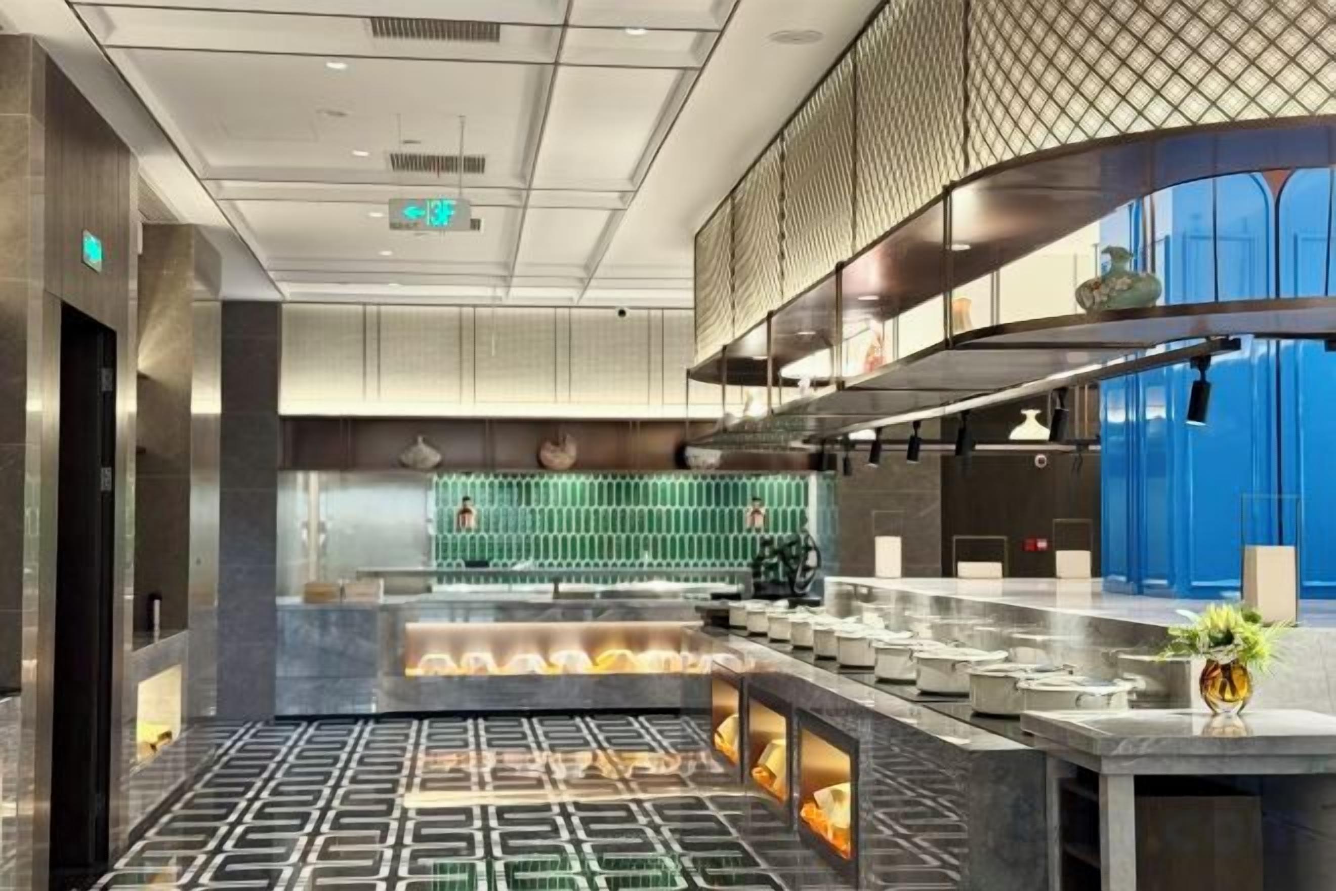A modern hotel lobby with a central bar area, seating arrangements, and a decorative fountain.