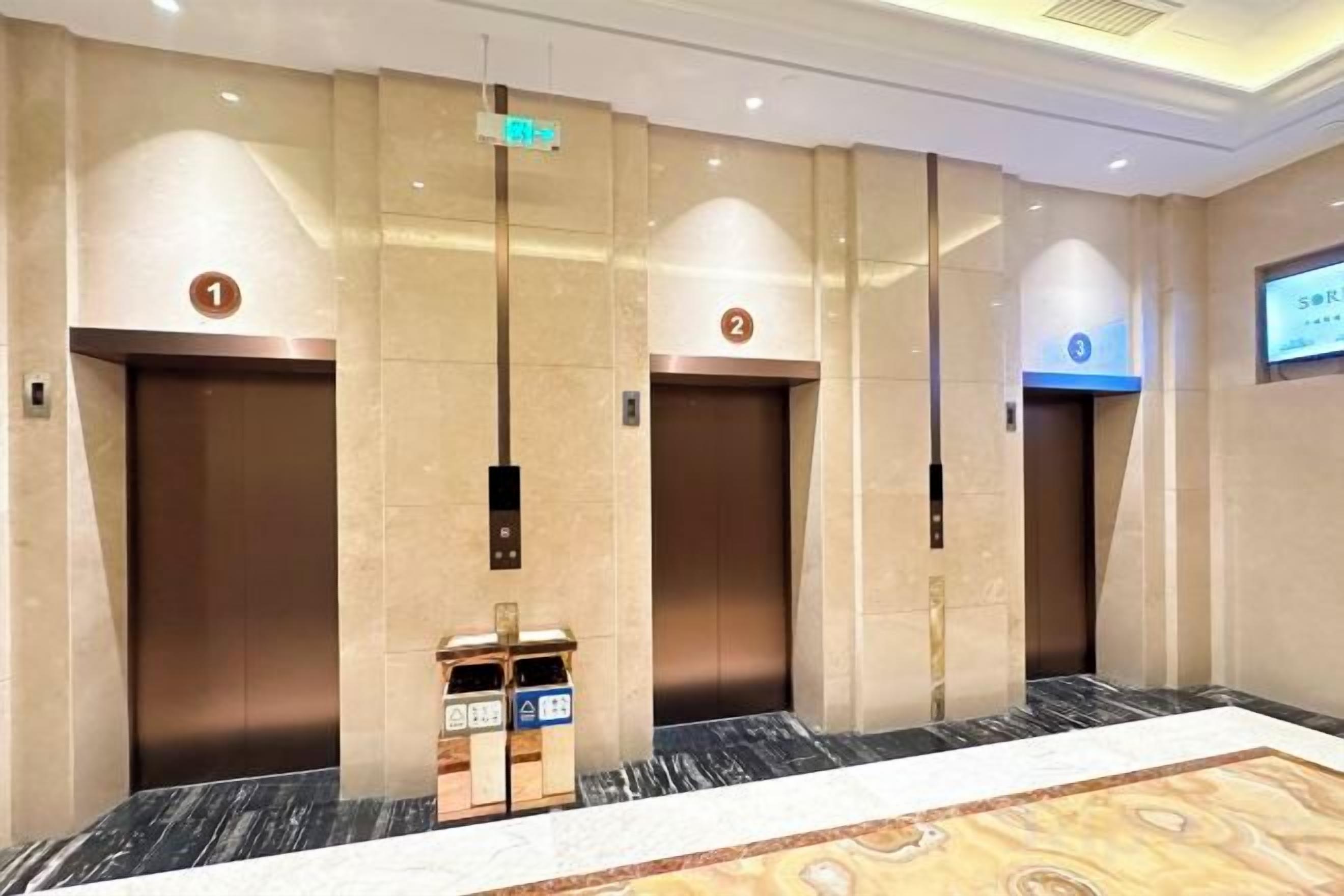 Um saguão de hotel com três elevadores, um balcão de recepção e piso coberto de carpete.