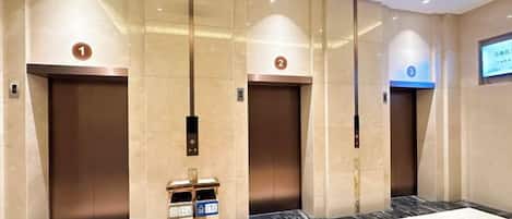 Um saguão de hotel com três elevadores, um balcão de recepção e piso coberto de carpete.