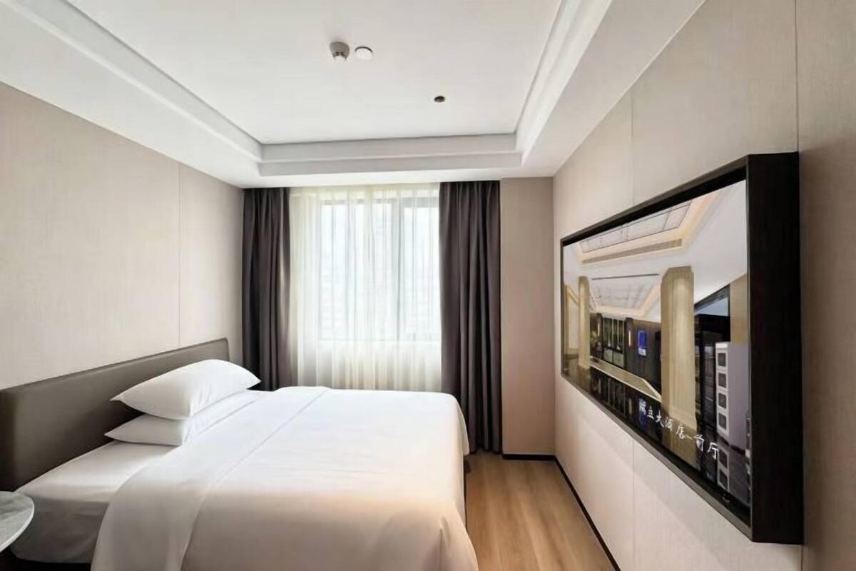 Habitación de hotel con cama, televisión, ventana con cortinas y una obra de arte colgada en la pared.