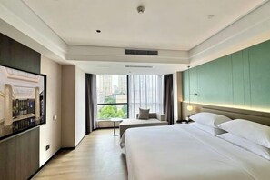Habitación de hotel con una cama grande, televisión, balcón y vistas a edificios, además de una pared de acento verde.
