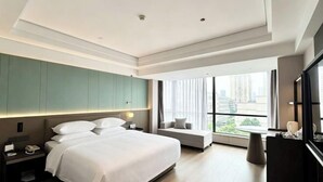 A modern hotel room with a large bed, a seating area, a desk, and a large window offering a city view. - Ruili Hotel (Rui'an)