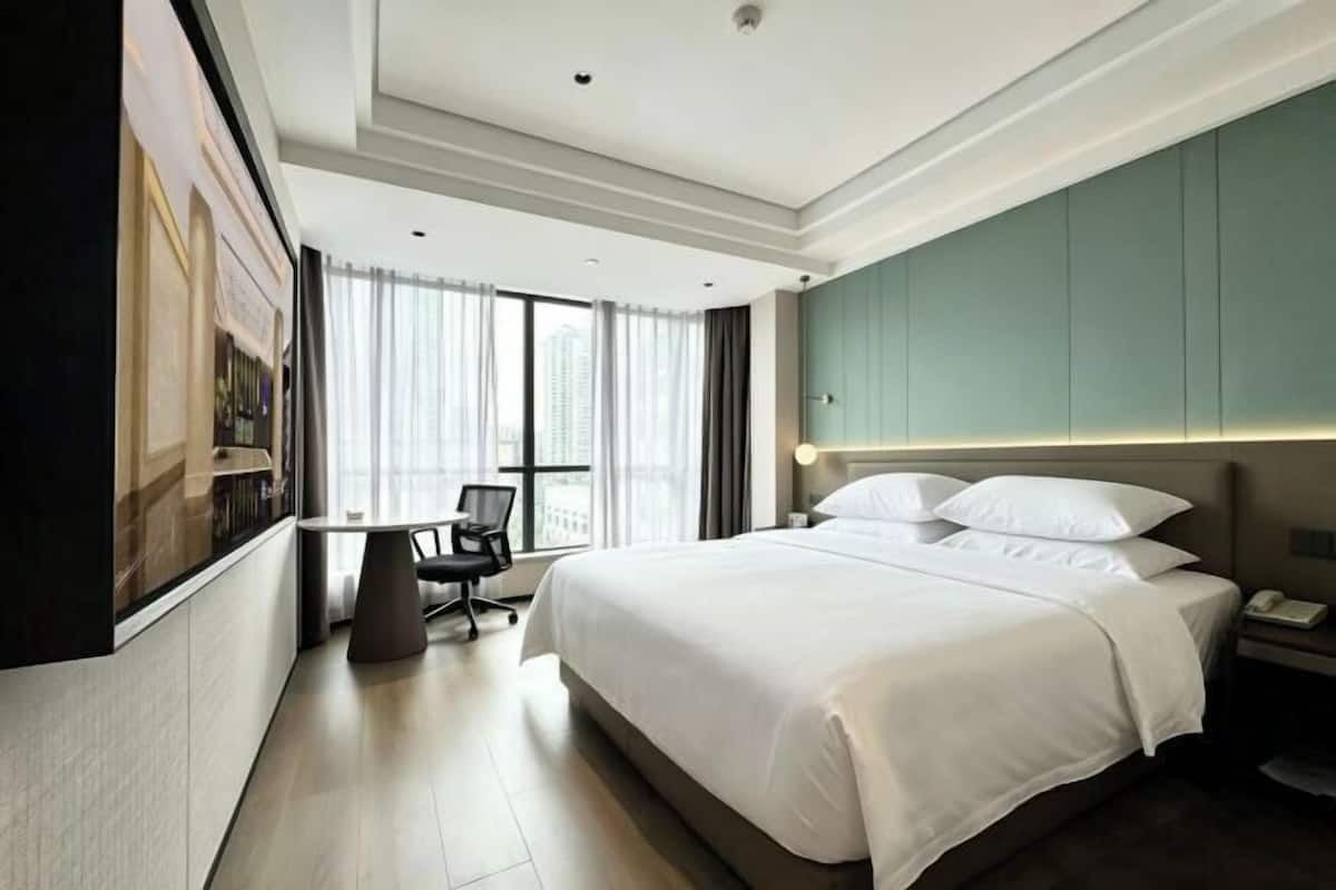 A modern hotel room with a large bed, a desk, and a chair.