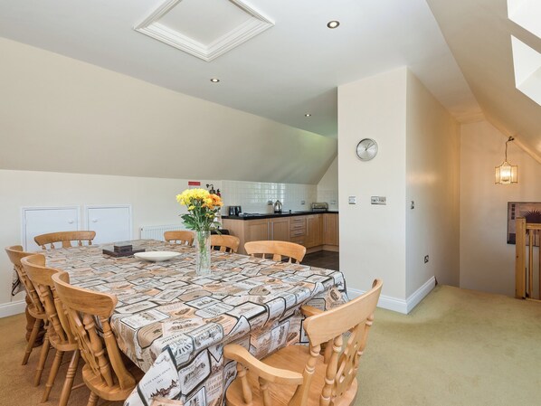 A dining area with a table covered in a patterned tablecloth, surrounded by wooden chairs. A vase with yellow flowers is on the table. - 4 bedroom accommodation in Horning, near Norwich (Horning, near Norwich)