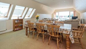 A spacious living area with a high ceiling, skylights, a dining table with chairs, a sofa, and a bookshelf. - 4 bedroom accommodation in Horning, near Norwich (Horning, near Norwich)