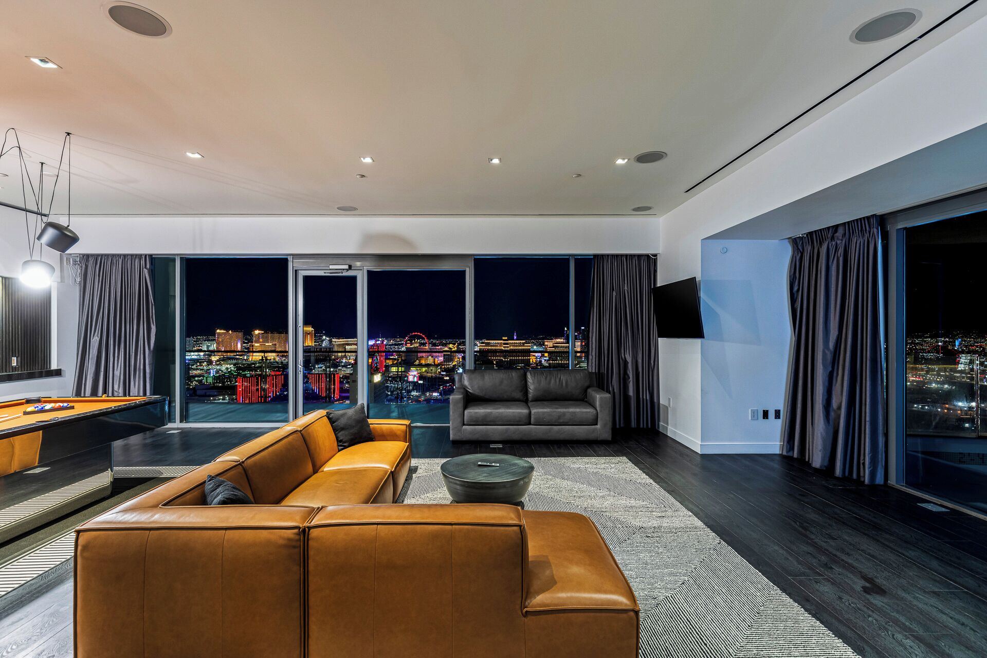 A modern living room with a pool table, leather sofa, and a large window with a city view.