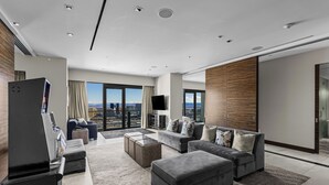 Ein modernes Wohnzimmer mit einer großen Sofagarnitur, einem Couchtisch und einem Flachbildfernseher. Ein großes Fenster bietet Blick auf die Stadt.