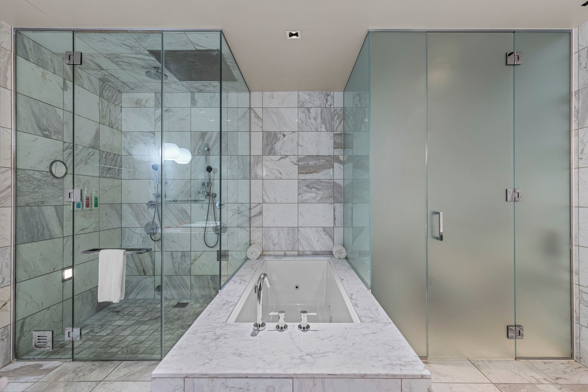 A modern bathroom with a glass-enclosed shower, a freestanding bathtub, and a glass door vanity.