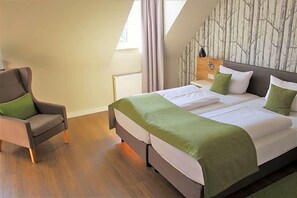 A bedroom with a bed, a chair, a window, and a wall with a tree pattern. - Eifelbräu (Bitburg)