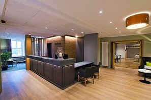 A modern reception area with a wooden reception desk, a seating area with chairs, and a view of the adjacent room. - Eifelbräu (Bitburg)