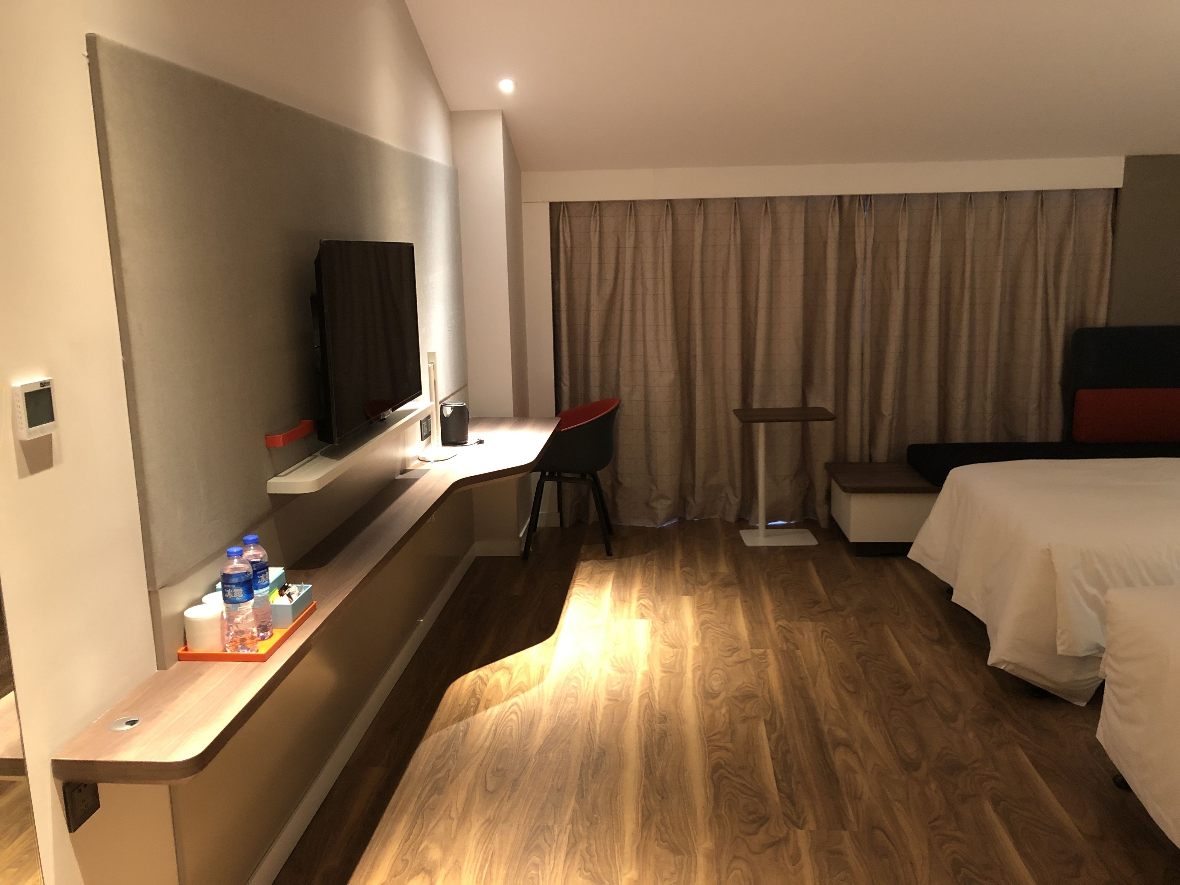 A hotel room with a bed, a desk with a chair, a TV, and a window with curtains.