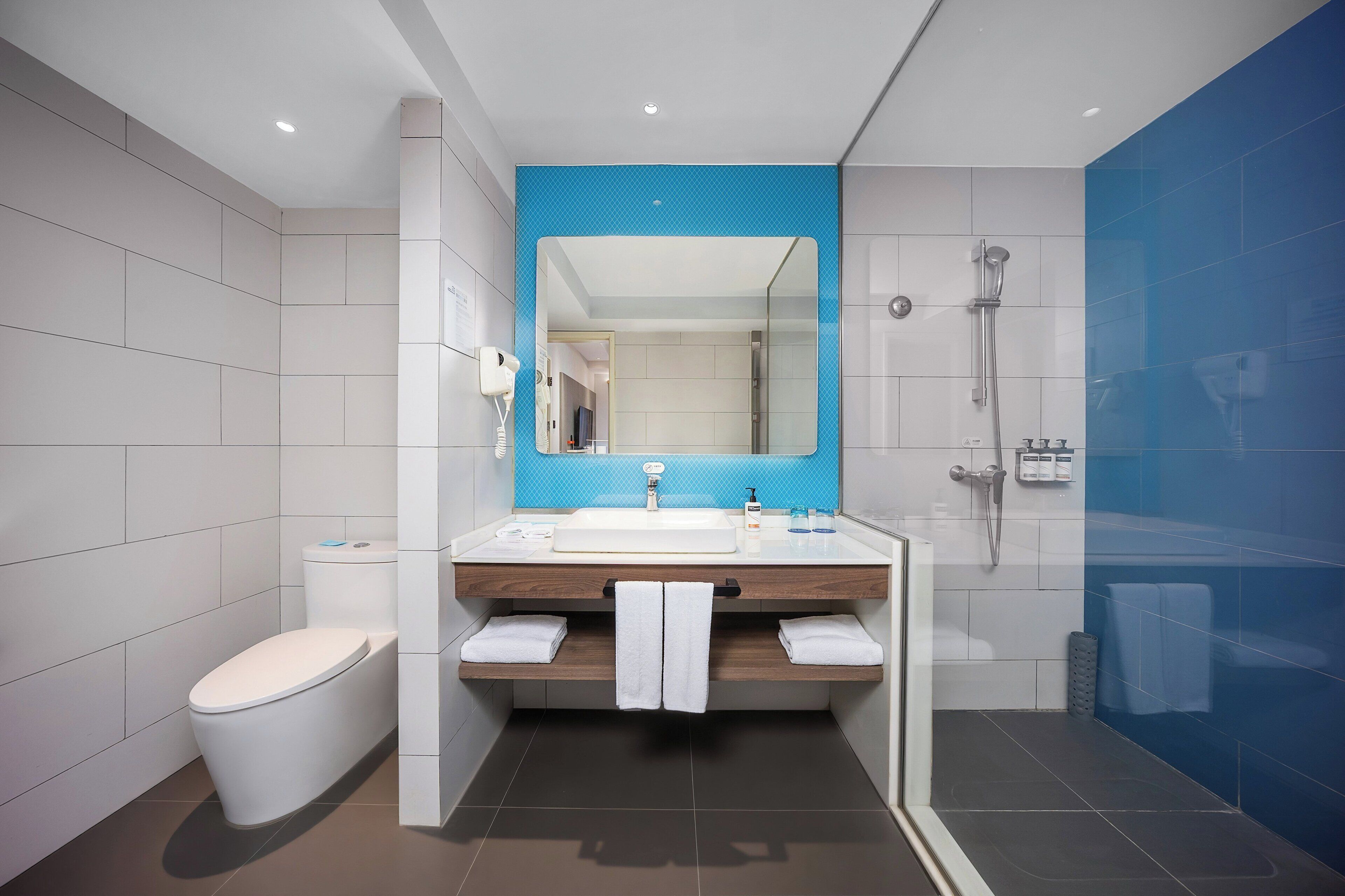 Un baño moderno con inodoro blanco, lavamanos con espejo azul y zona de ducha.
