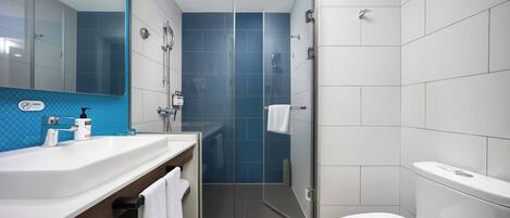 A modern bathroom with a white sink, mirror, and toilet, a glass-enclosed shower, and blue-tiled walls.