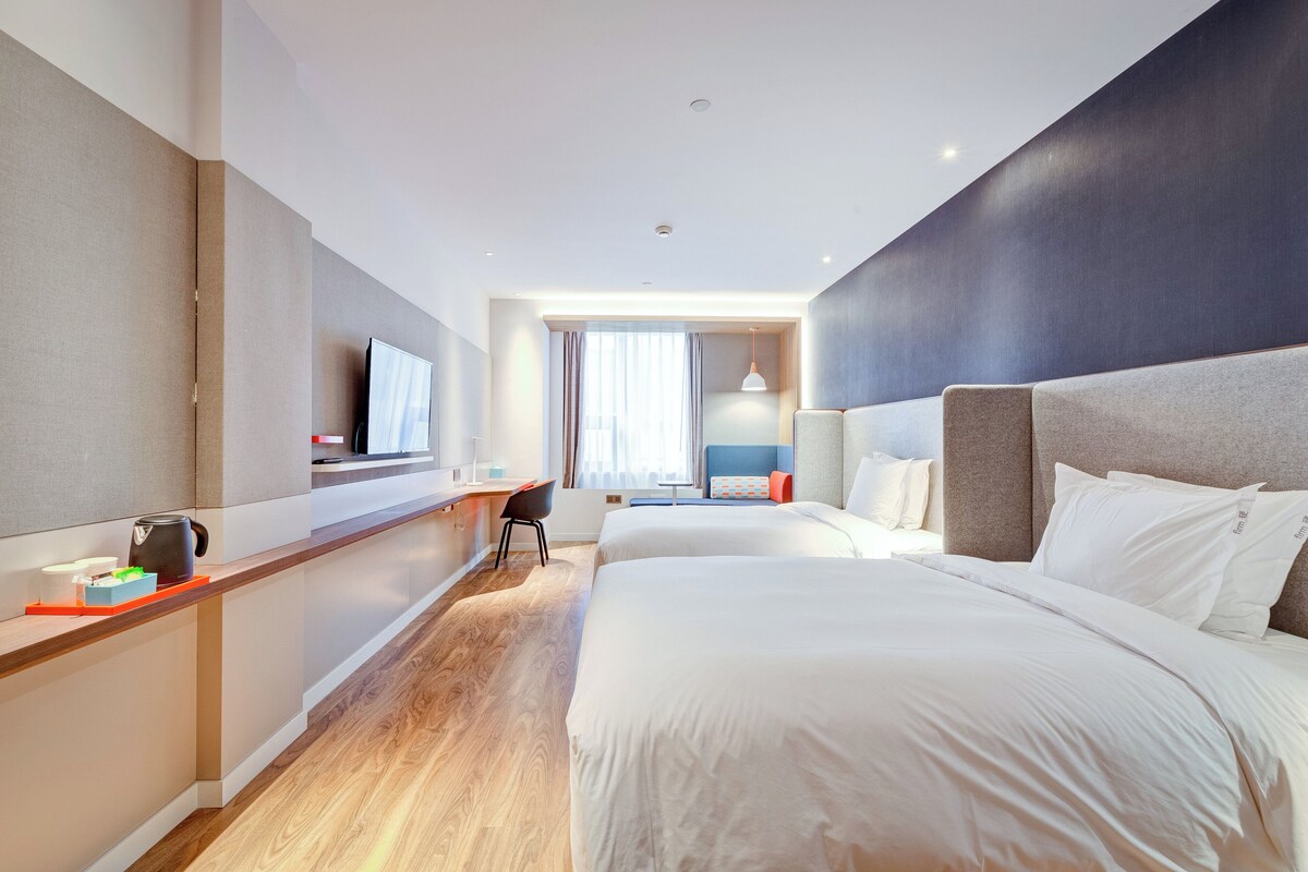 Ein Hotelzimmer mit Bett, Schreibtisch, Stuhl, Fernseher und Fenster.