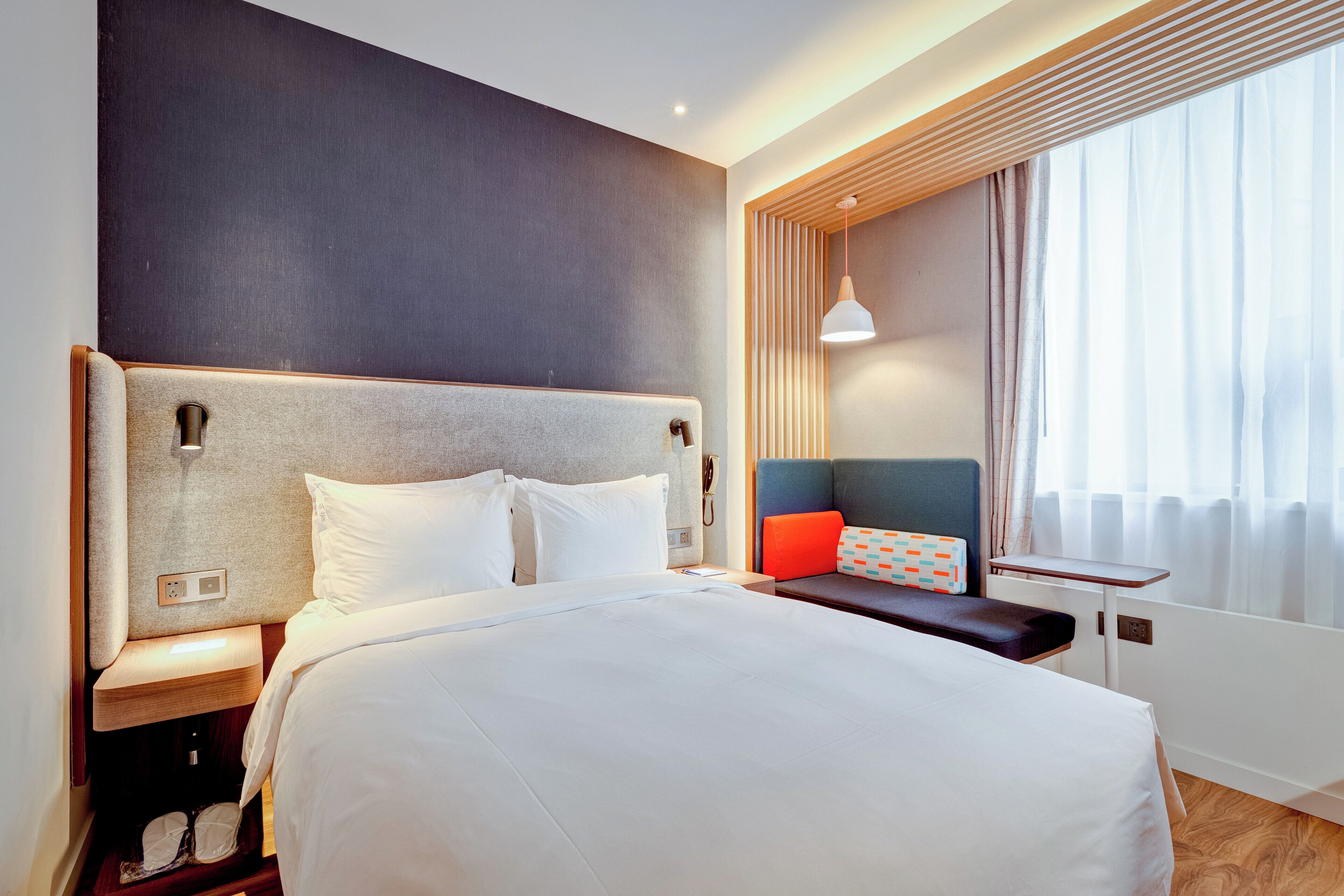 A hotel room with a large bed, bedside tables, a desk, and a window with curtains.