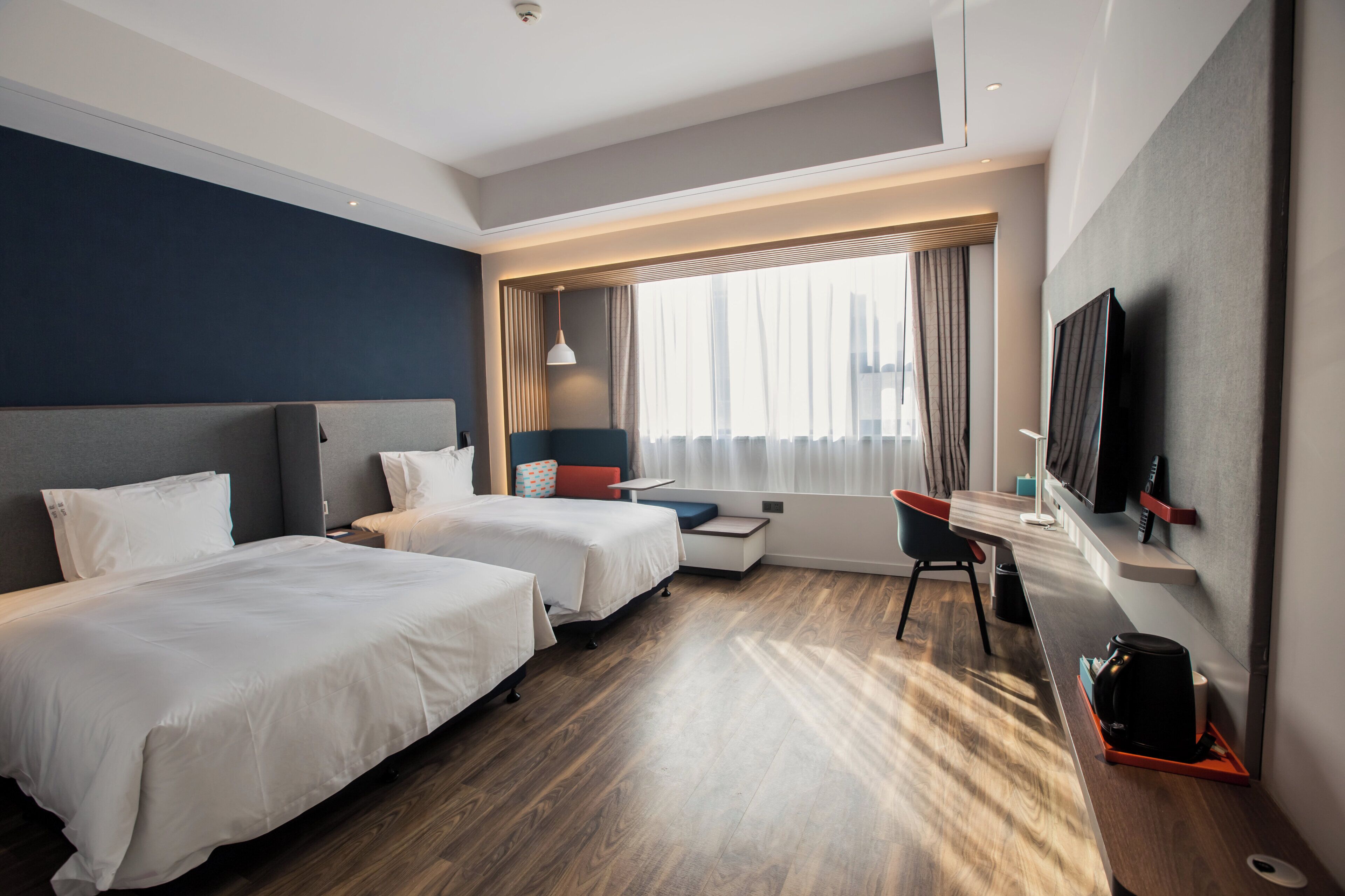 A hotel room with two beds, a desk, a chair, a TV, and a window with curtains.