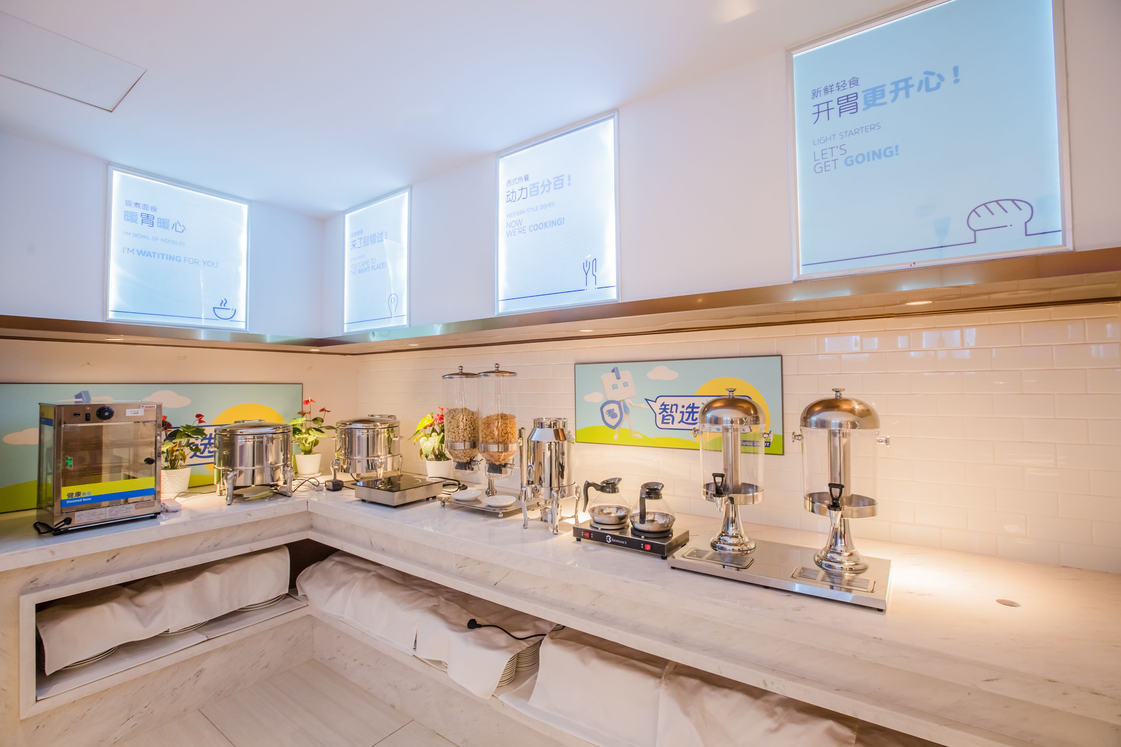 A modern kitchen with a long counter, various cooking appliances, and a large window with a view of the sky.