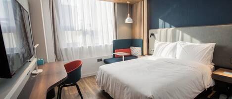Habitación de hotel con cama, escritorio, silla, televisor y ventana con cortinas.