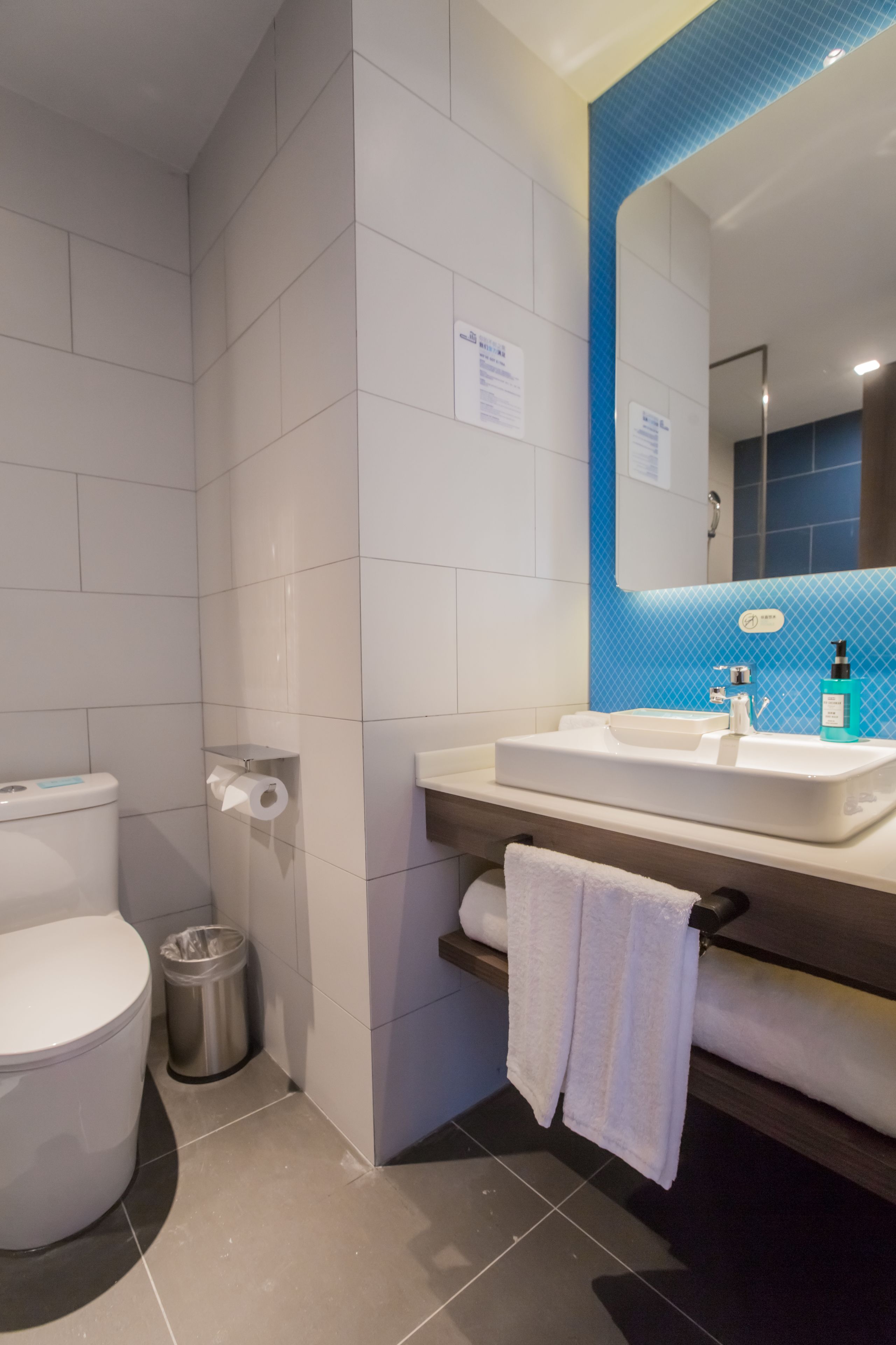 A modern bathroom with a white toilet, a sink with a mirror above it, and a trash can.