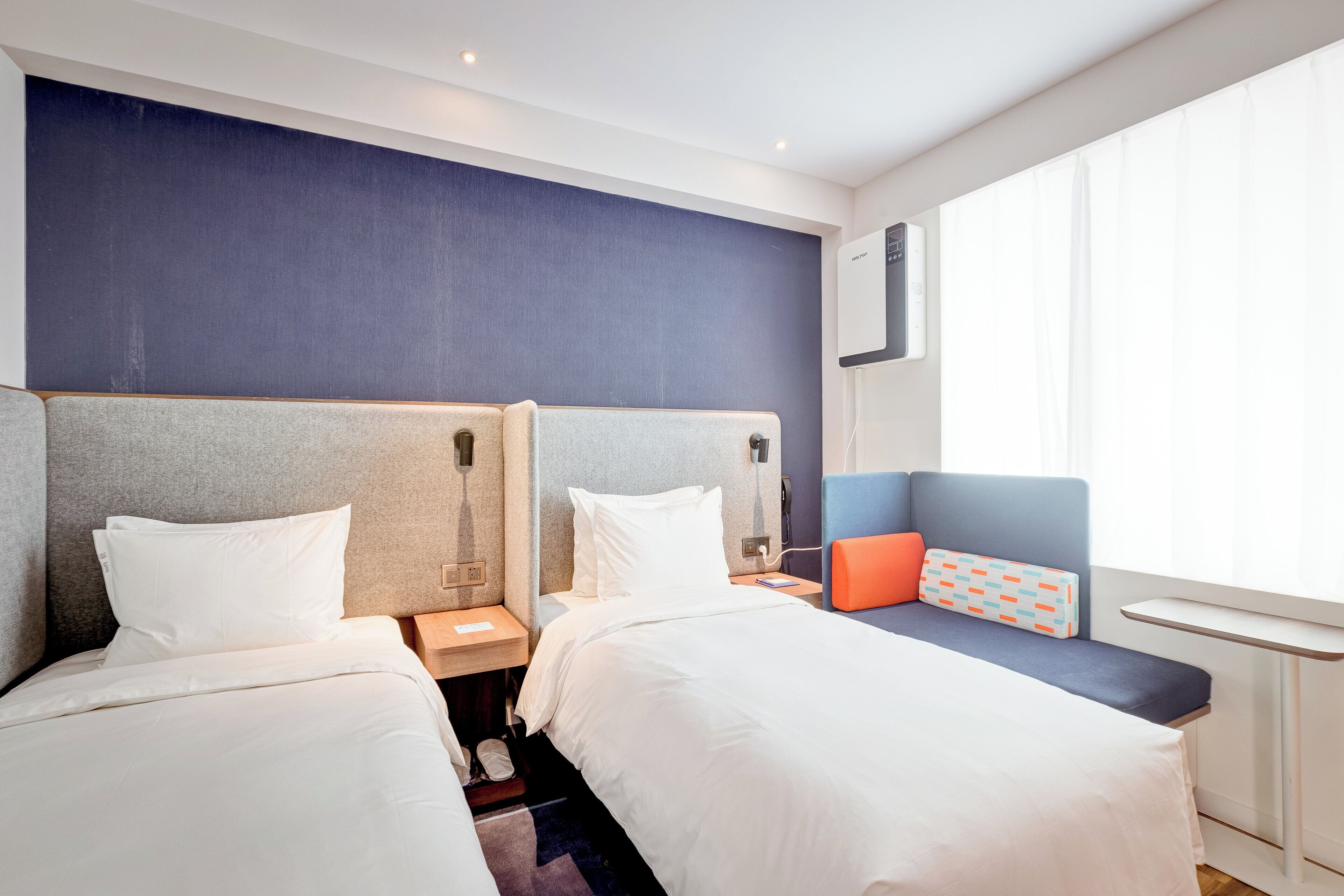 A hotel room with two beds, a nightstand, a small table, and a window with curtains.
