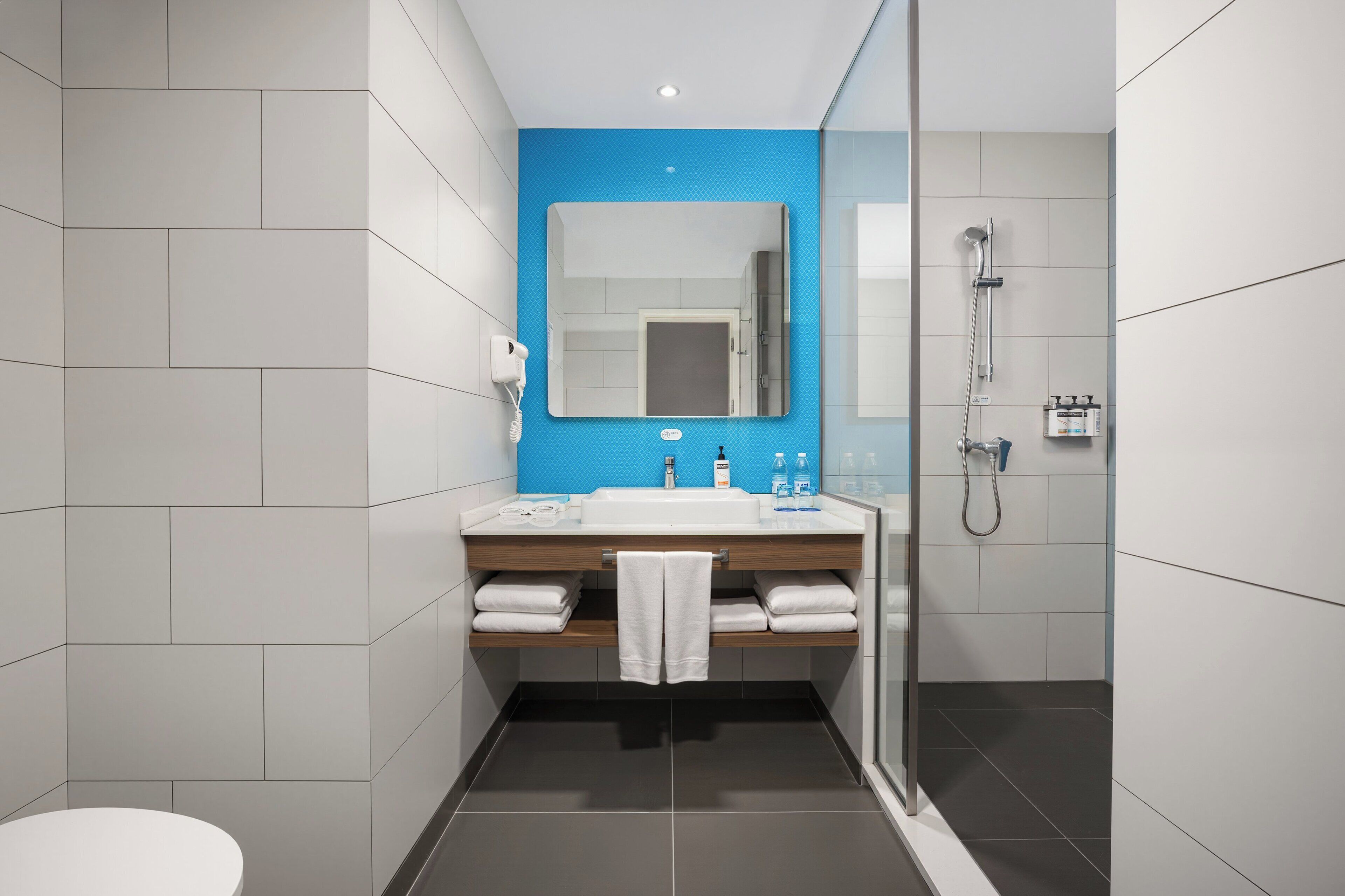 A modern bathroom with a white sink, blue accent wall, and a glass shower enclosure.